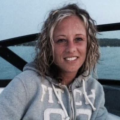 Melissa sitting on the boat wearubg a hoodie, with the lake behind her on a sunny day.